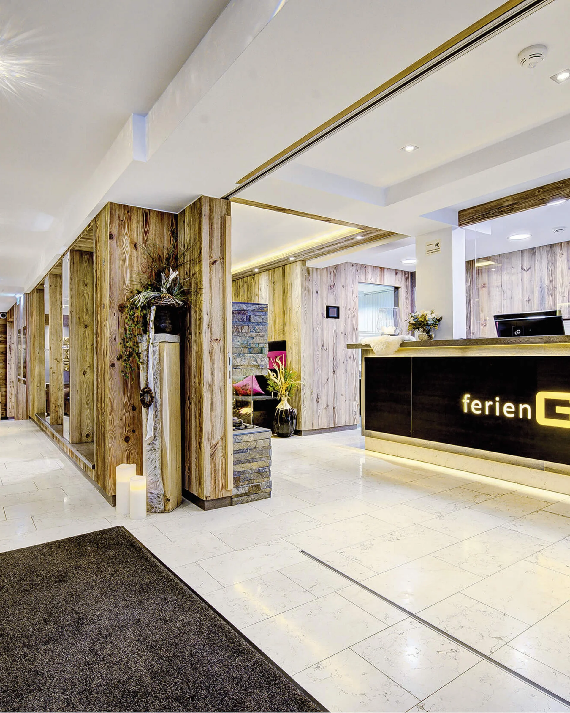 Ferienglück und Alpenland | Ihre stilvollen Hotels in Ischgl Heller Hotelrezeption mit Holzverkleidung und beleuchtetem FerienGlück-Schriftzug
