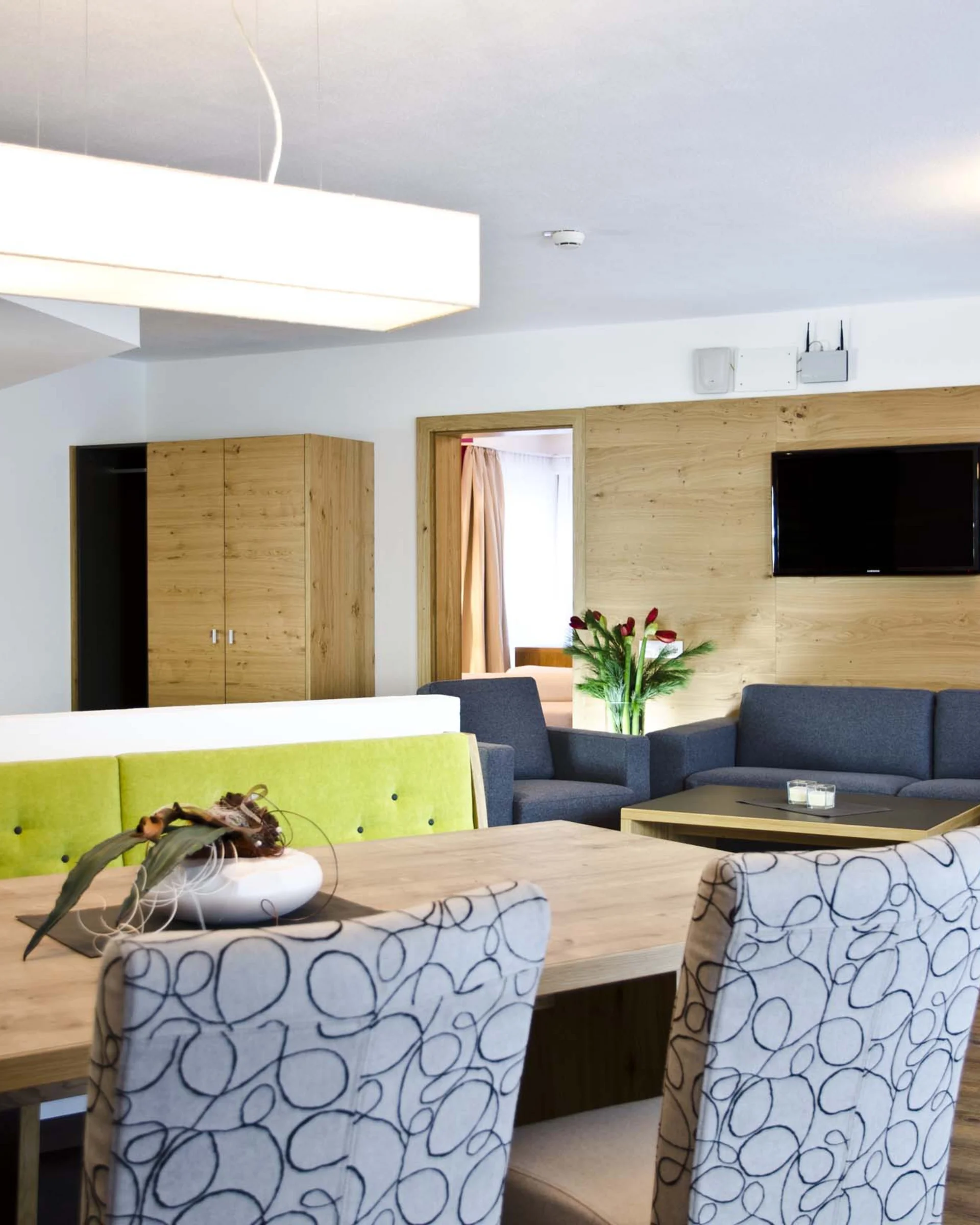 Ferienglück und Alpenland | Ihre stilvollen Hotels in Ischgl Modernes Wohnzimmer mit Esstisch, grüner Bank, Sesseln und blauem Sofa