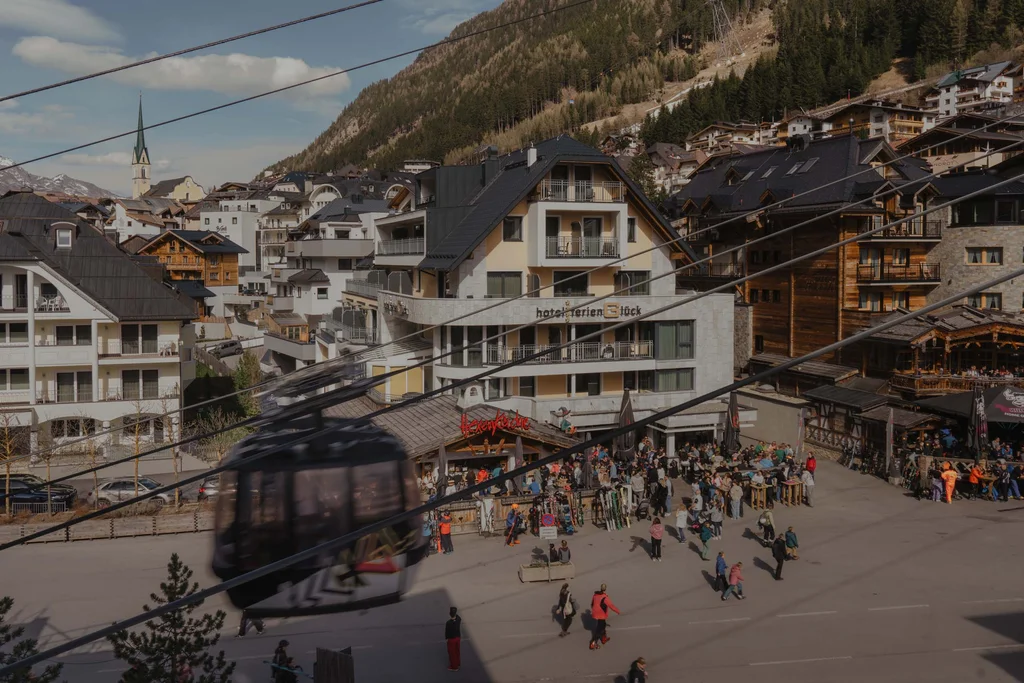 Ferienglück und Alpenland | Ihre stilvollen Hotels in Ischgl Bergdorf mit Seilbahnkabine, Bergkulisse, Hotels und vielen Menschen