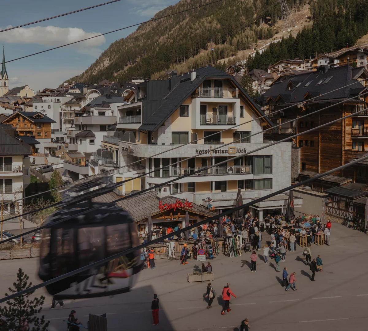 Ferienglück und Alpenland | Ihre stilvollen Hotels in Ischgl Bergdorf mit Seilbahnkabine, Bergkulisse, Hotels und vielen Menschen