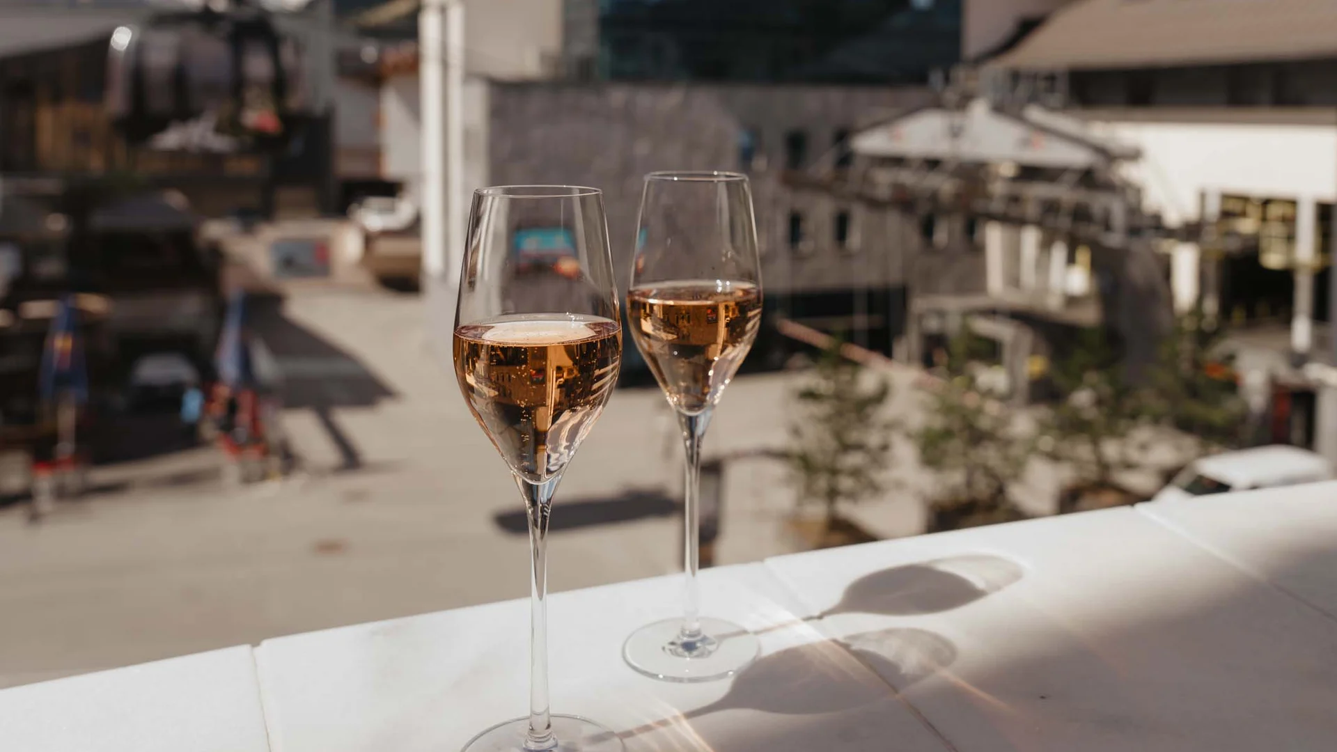 Ferienglück und Alpenland | Ihre stilvollen Hotels in Ischgl Zwei gefüllte Weingläser auf einer Terrasse mit Bergdorf im Hintergrund