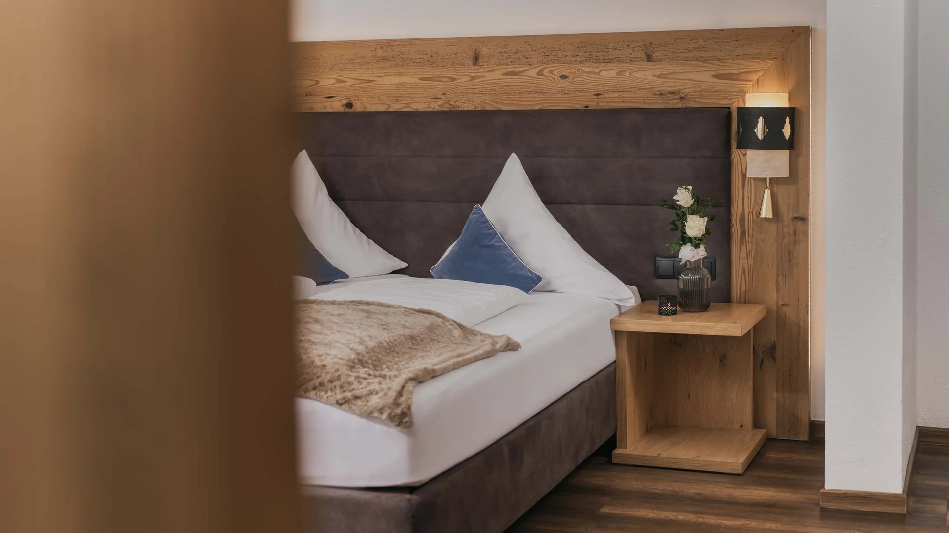 Ferienglück und Alpenland | Ihre stilvollen Hotels in Ischgl Gemütliches Hotelzimmer mit Doppelbett, Holzkopfteil und Nachttisch