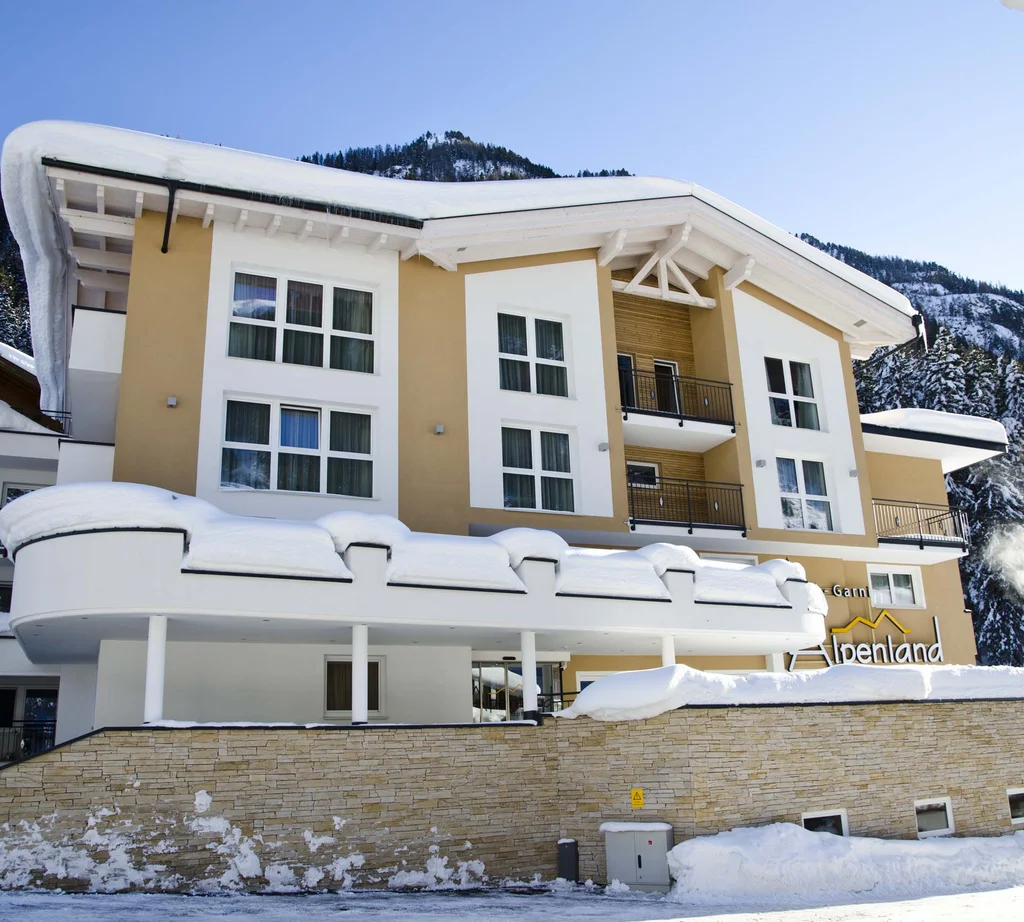 Ferienglück und Alpenland | Ihre stilvollen Hotels in Ischgl Verschneites Hotel Alpenland vor bewaldeten Bergen