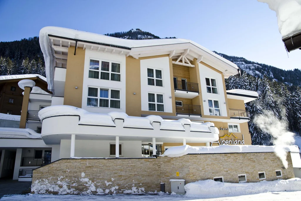 Ferienglück und Alpenland | Ihre stilvollen Hotels in Ischgl Verschneites Hotel Alpenland vor bewaldeten Bergen
