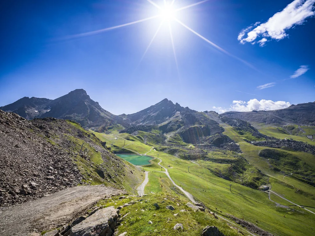 Ferienglück und Alpenland | Ihre stilvollen Hotels in Ischgl Sonnige Berglandschaft mit Wanderwegen, grünen Hängen und kleinem Bergsee