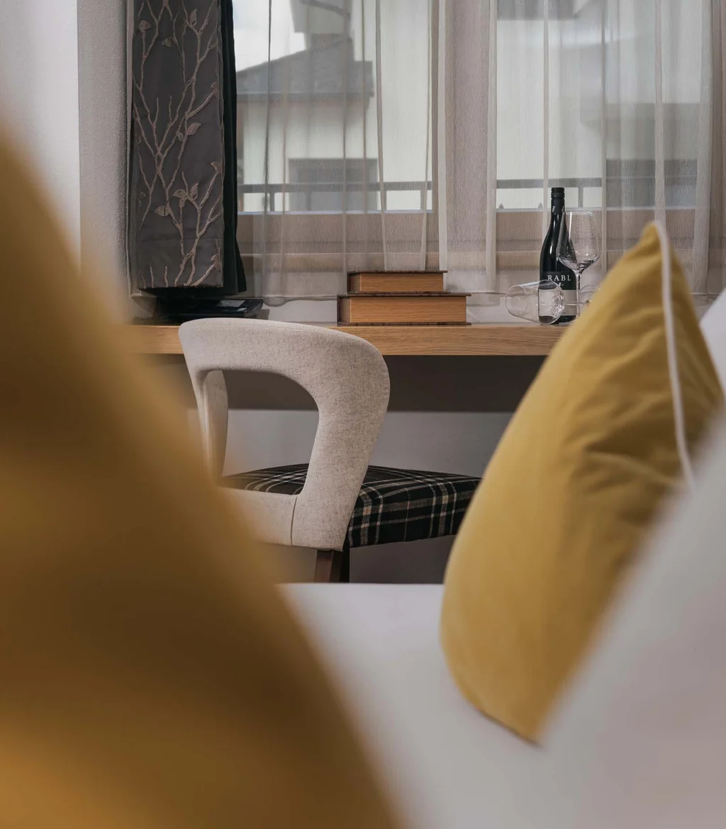 Ferienglück und Alpenland | Ihre stilvollen Hotels in Ischgl Gemütliches Zimmer mit gelben Kissen, Schreibtisch und Sessel am Fenster