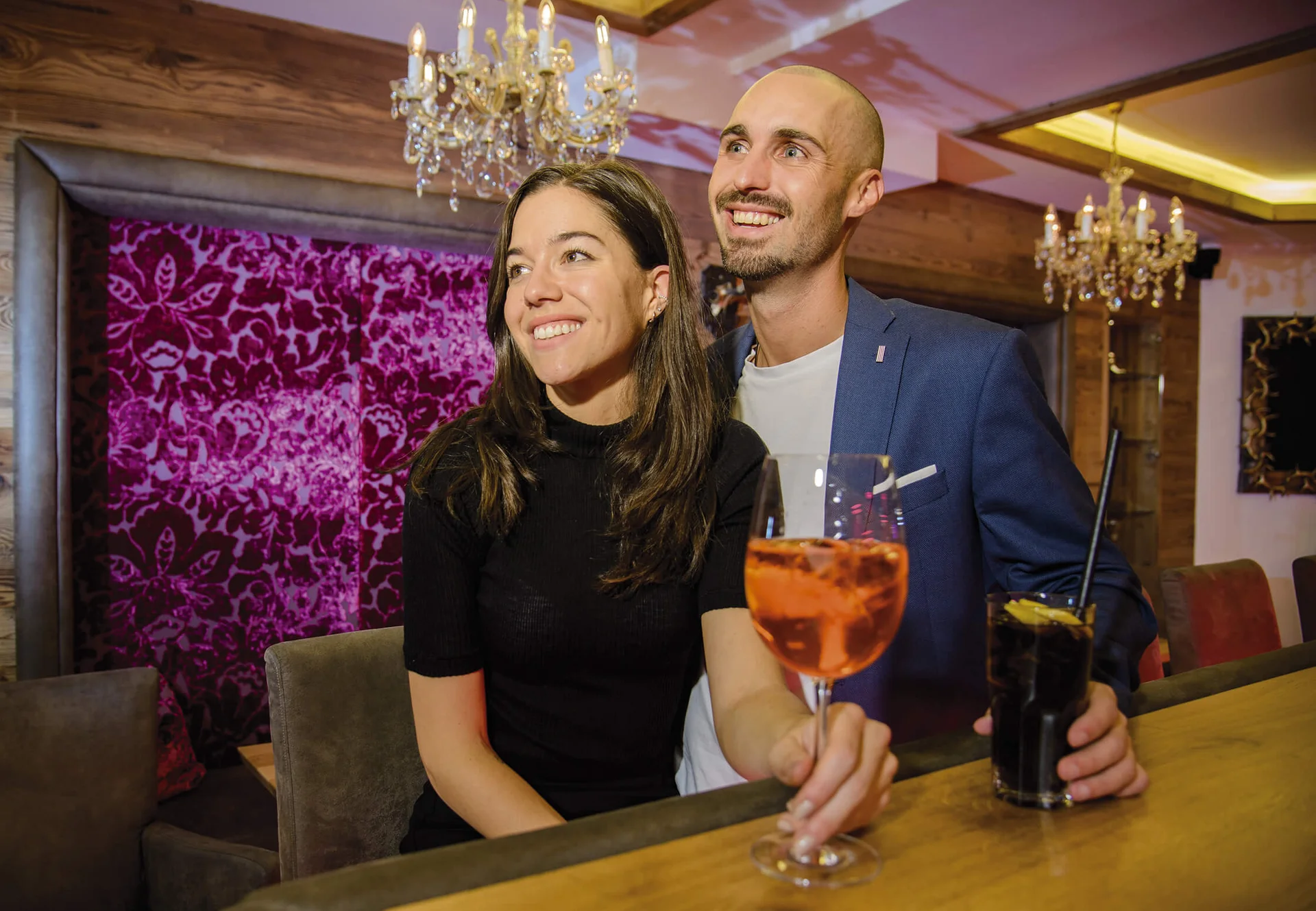 Ferienglück und Alpenland | Ihre stilvollen Hotels in Ischgl Paar mit Cocktails in einer stilvollen Bar mit Kronleuchtern
