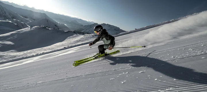 Ferienglück und Alpenland | Ihre stilvollen Hotels in Ischgl Skifahrer fährt über eine verschneite Piste vor alpiner Bergkulisse