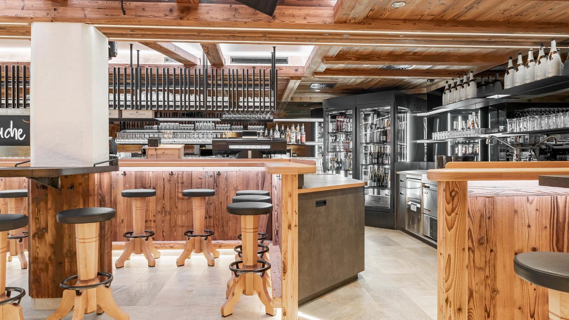 Ferienglück und Alpenland | Ihre stilvollen Hotels in Ischgl Rustikale Bar mit Holzverkleidung, Hockern, Regalen und Getränkekühlern