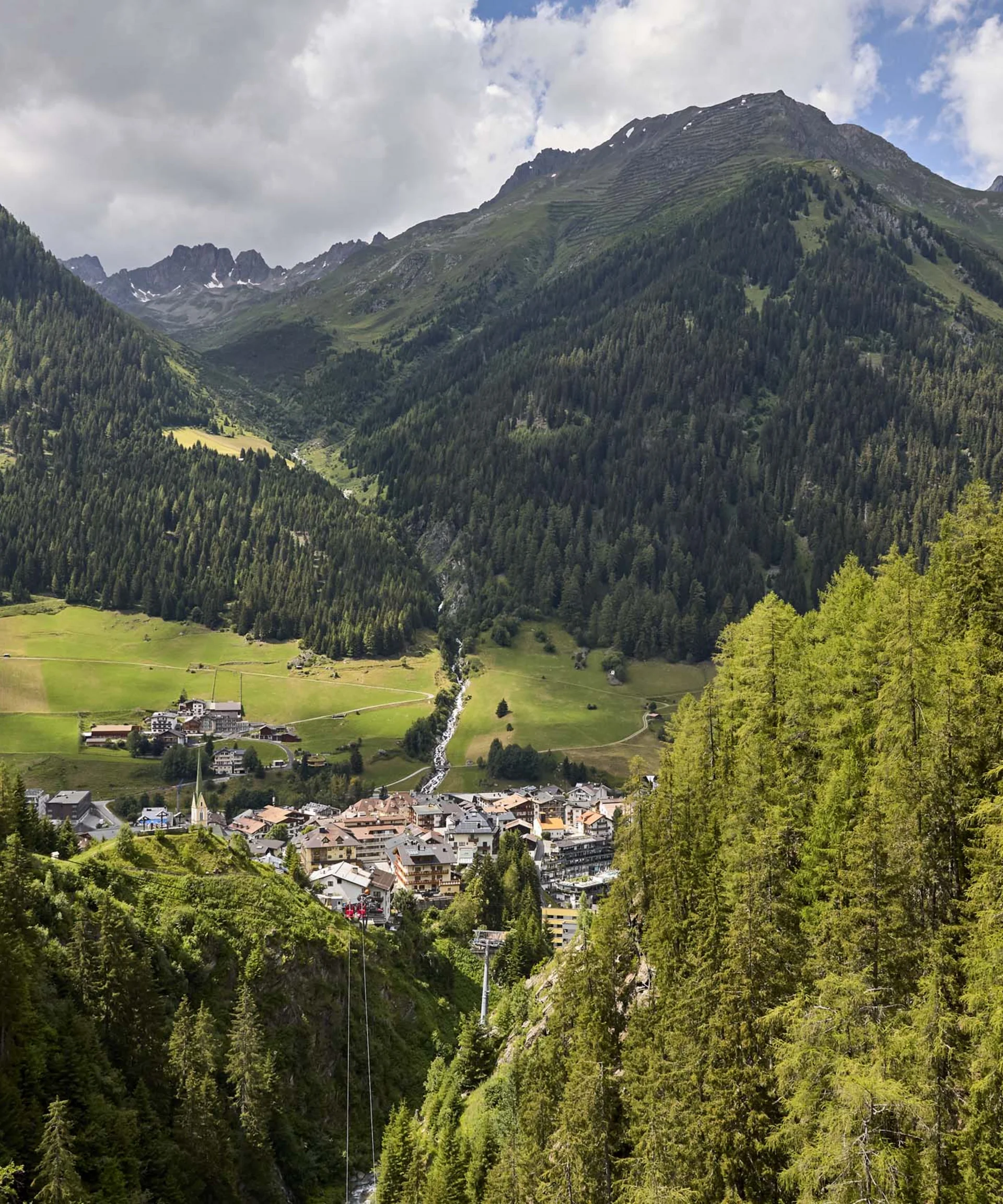 Ferienglück und Alpenland | Ihre stilvollen Hotels in Ischgl Bergdorf in einem grünen Tal, umgeben von bewaldeten Berghängen und hohen Gipfeln