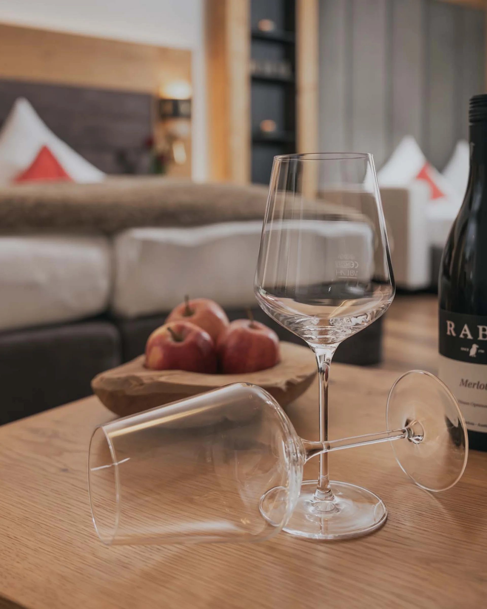 Ferienglück und Alpenland | Ihre stilvollen Hotels in Ischgl Weinflasche, zwei Weingläser und Äpfel auf Holztisch vor einem Sofa