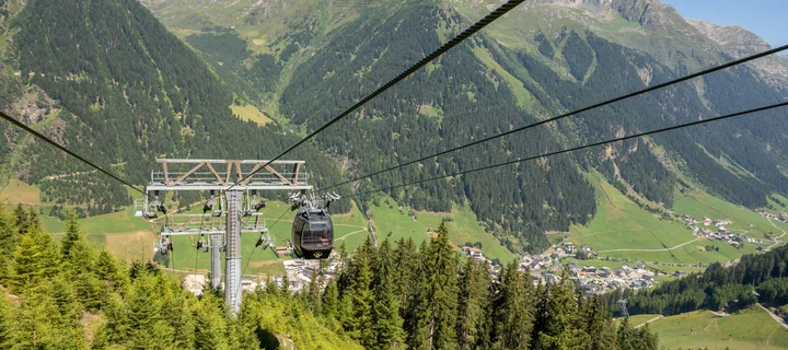 Ferienglück und Alpenland | Ihre stilvollen Hotels in Ischgl Gondelbahn über alpines Tal mit Berglandschaft und bewaldeten Hängen